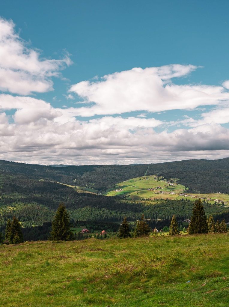 A vertical shot of hills covered in greenery under a blue cloudy sky and sunlight